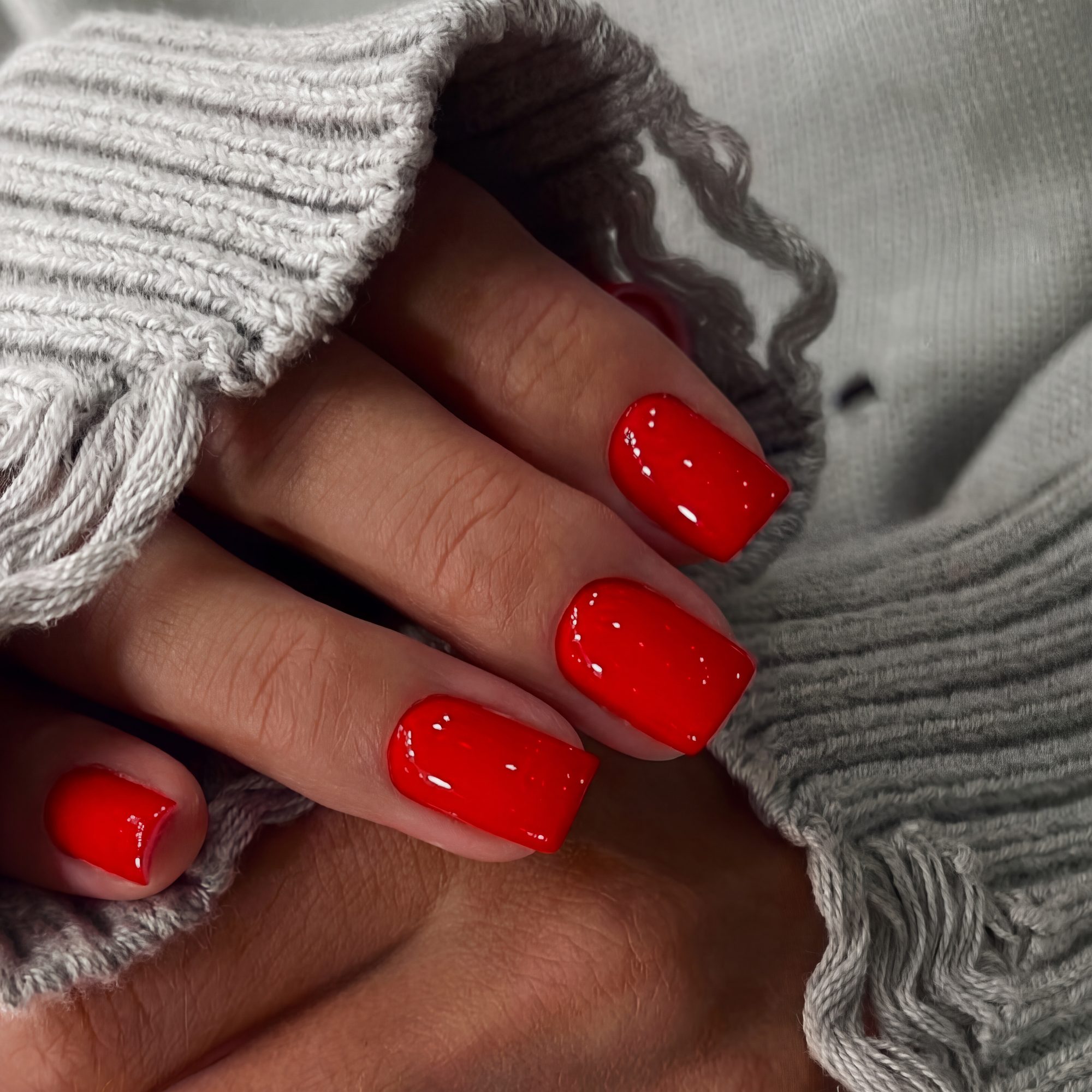 Manicura roja brillante sobre un jersey de punto gris